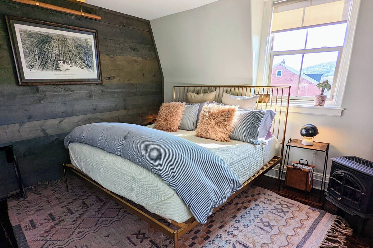 A bedroom with a bed, a rug, a framed picture, a window, and a radiator.