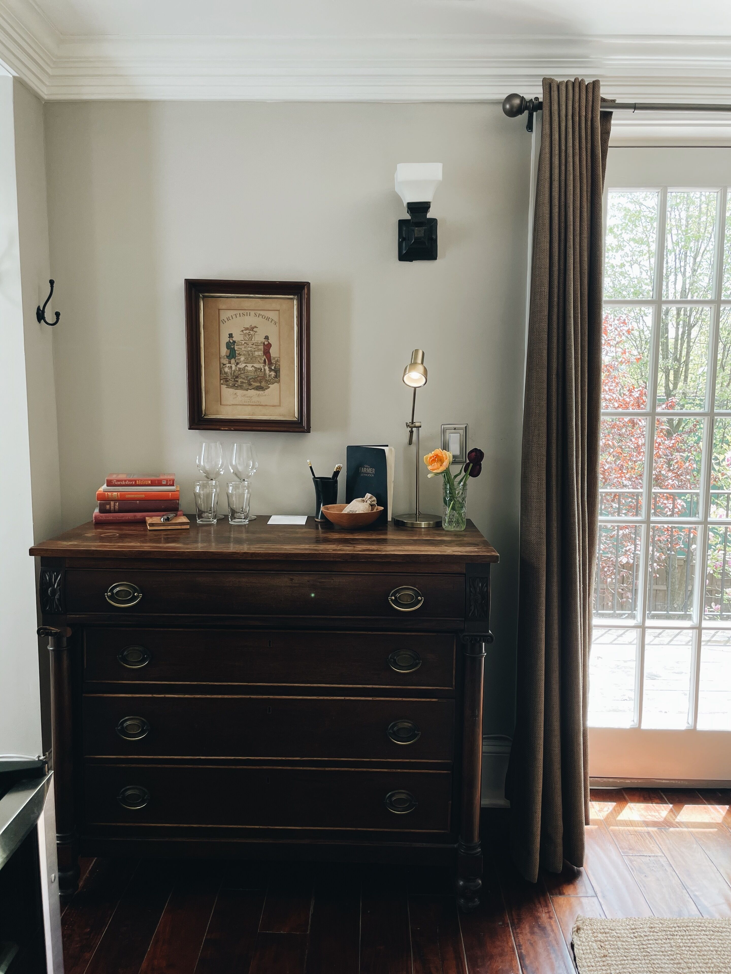 A wooden dresser with drawers, a framed picture on the wall, a lamp, and a window with curtains.