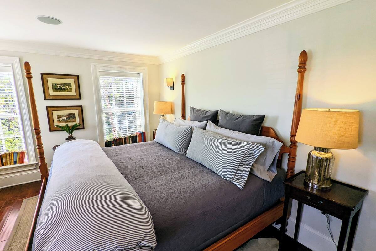 A neatly made bed with a grey bedspread and striped pillows, a wooden headboard, and a bedside table with a lamp.