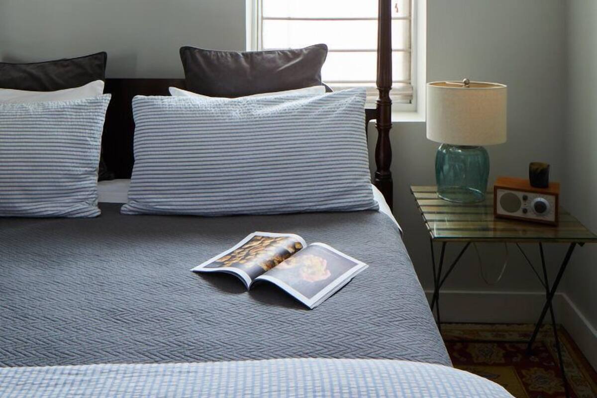 A bedroom with a bed, pillows, a magazine, a lamp, and a radio on a side table.