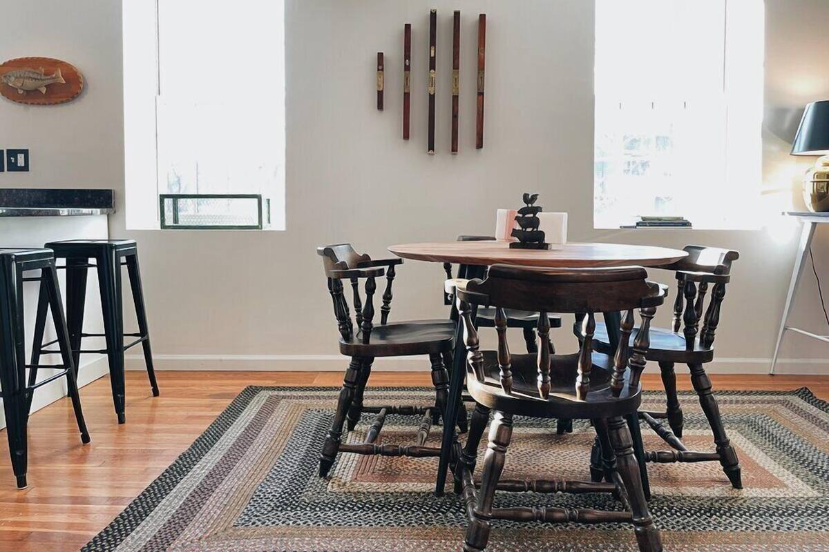 A dining area with a round table and six chairs, a kitchen area with a counter and stools, and a large window providing natural light.