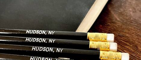 Un libro con el título 'JAMES & SONS' y cuatro lápices con la etiqueta 'HUDSON, NY' sobre una superficie de madera.