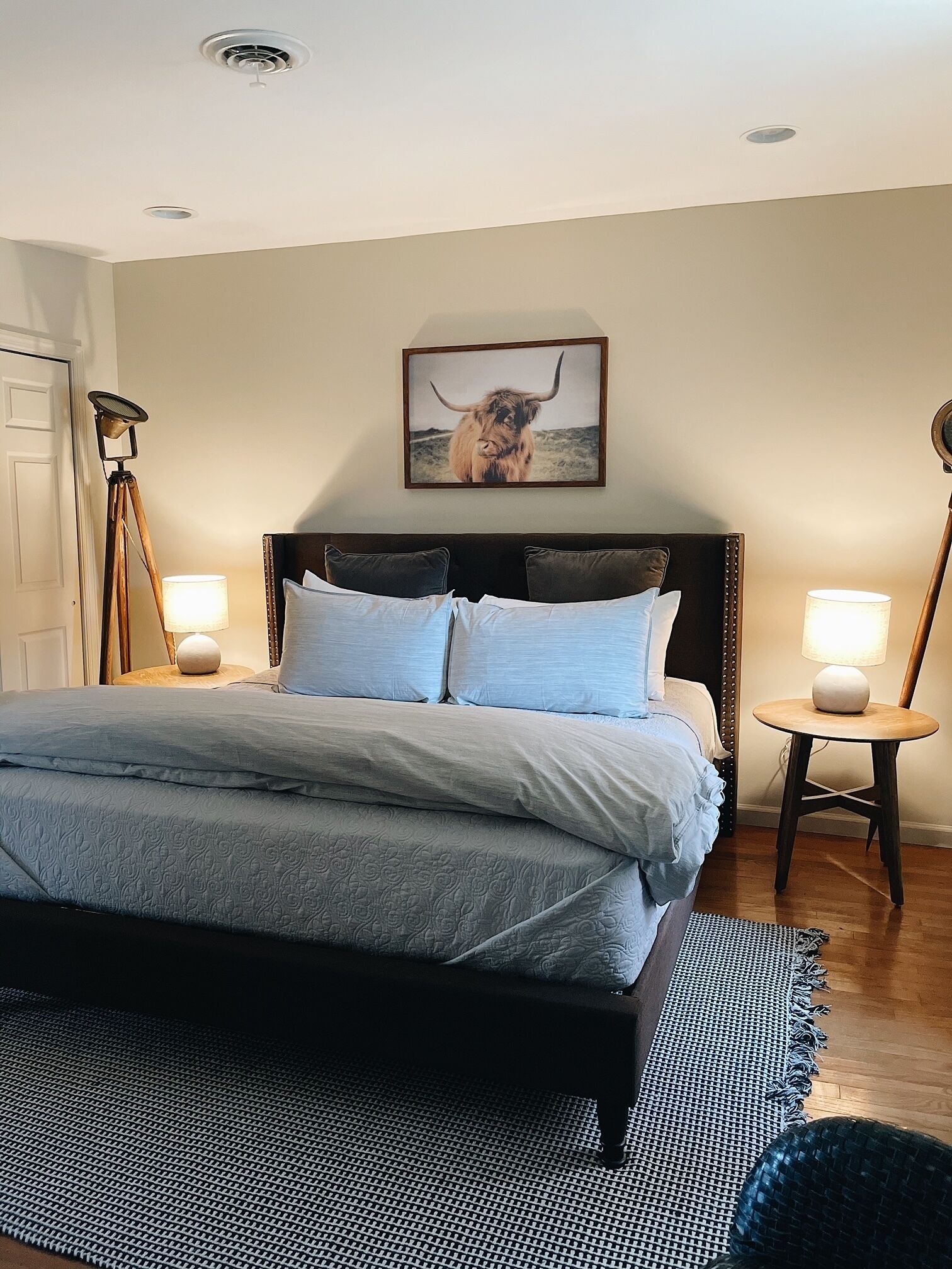 A bedroom with a large bed, two bedside lamps, a framed picture on the wall, and a floor lamp.