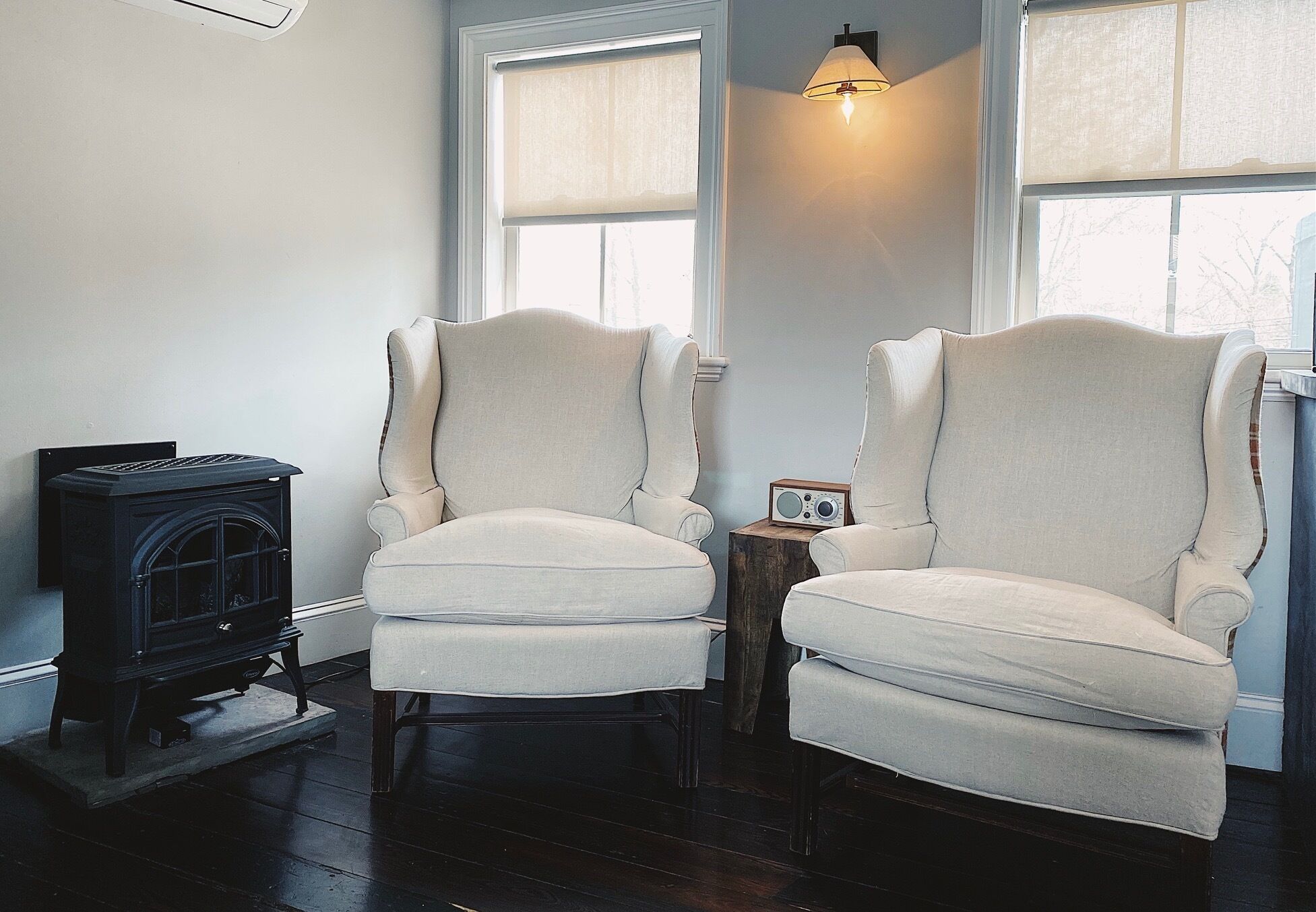 Two white armchairs, a black wood-burning stove, and a small wooden table with a radio.