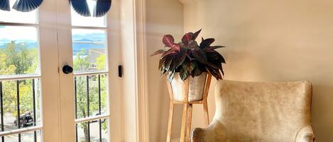 A room with a wooden floor, a beige armchair, a potted plant, and a view through a door with blinds.