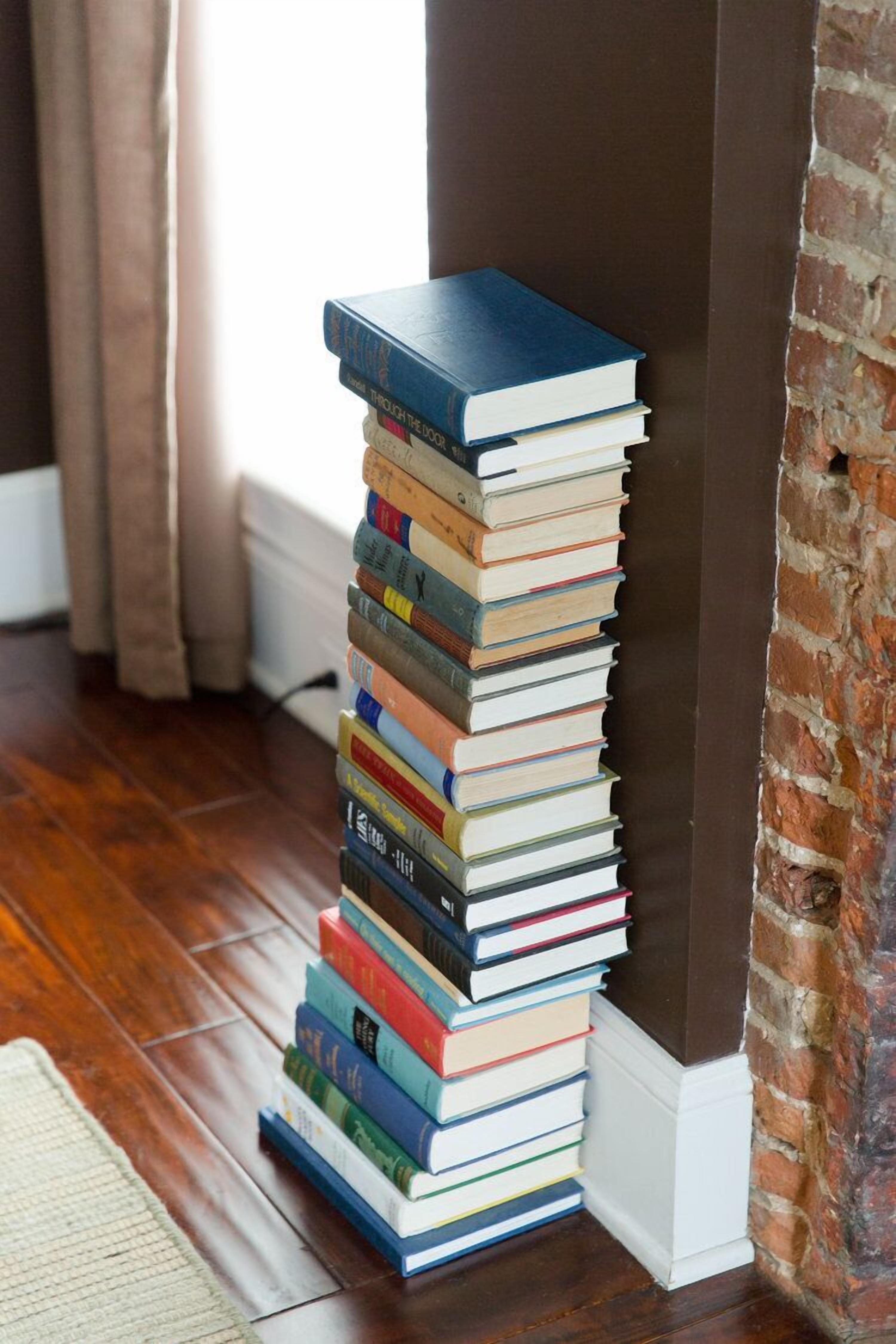 Ein Stapel Bücher an einer Wand in einem Raum mit Holzboden und einer Ziegelwand.