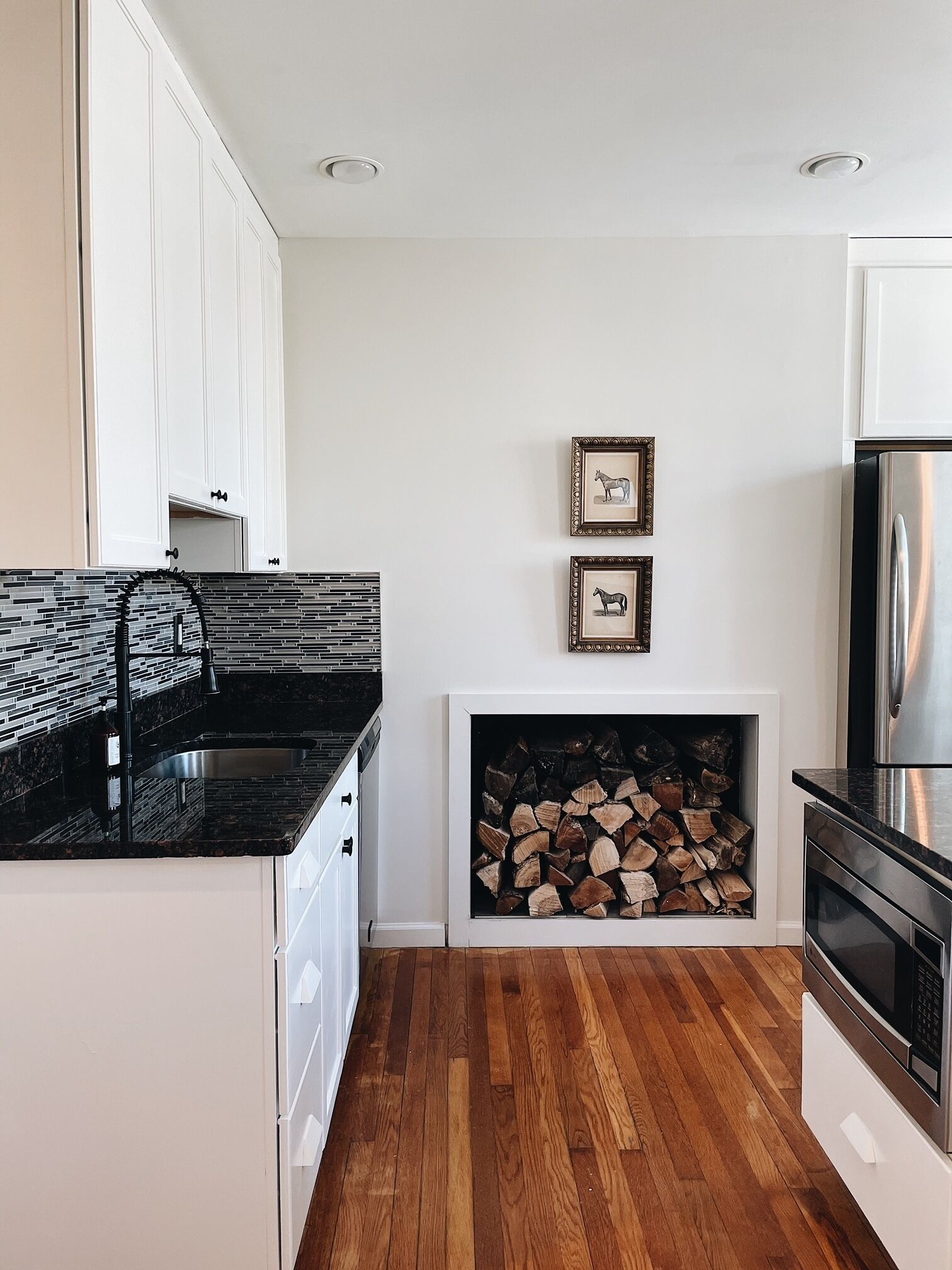 Una cocina moderna con armarios blancos, encimera negra y chimenea integrada.