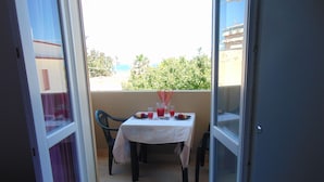 Un balcon ouvert avec une table dressée pour deux personnes, agrémentée d’une nappe blanche, de deux chaises et d’une petite table sur laquelle on trouve un verre de jus de fruits, une assiette de fraises et un verre d’eau.