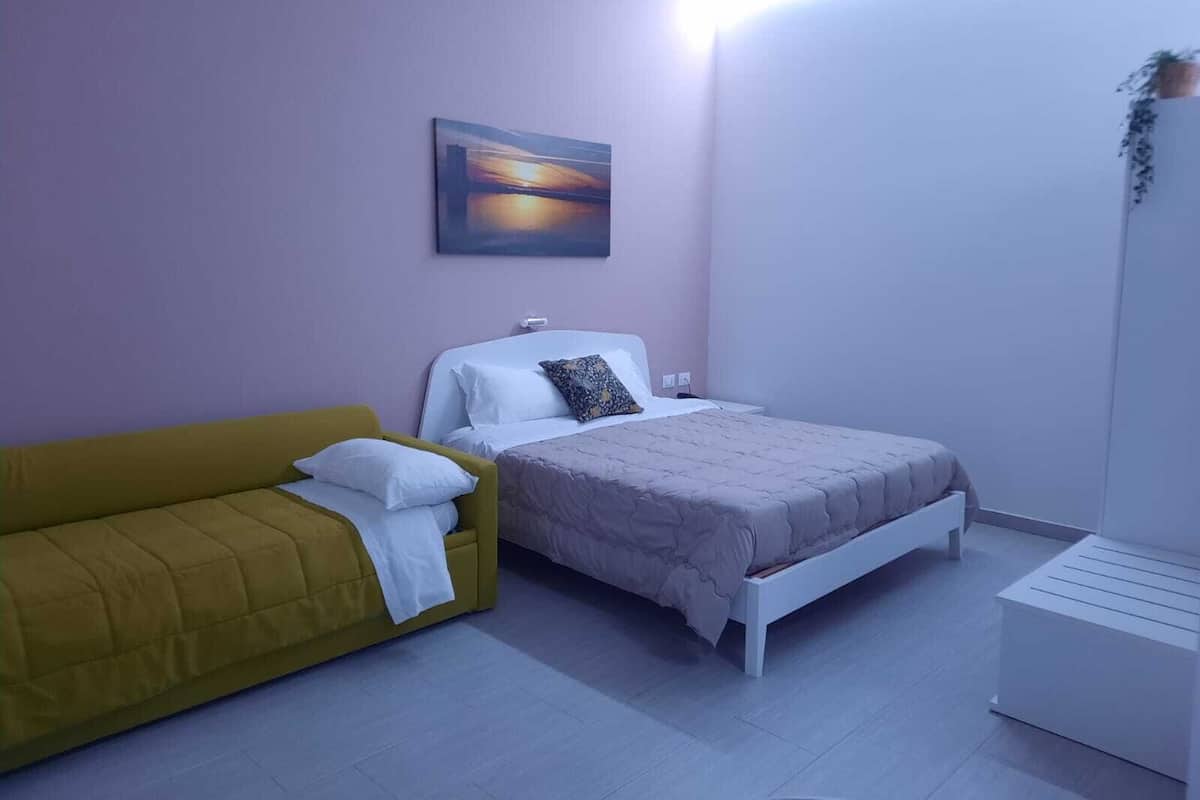 A bedroom with a bed, a yellow sofa, and a white bedside table.