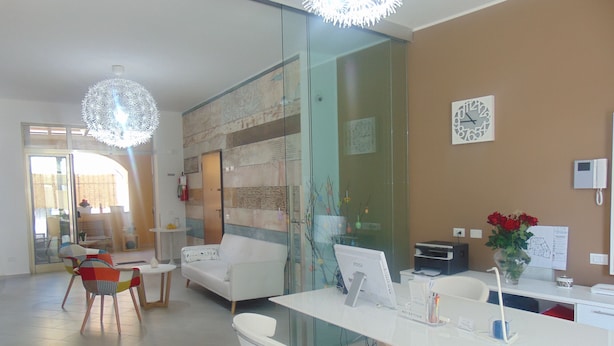 Un espace d’accueil moderne avec un bureau blanc, un ordinateur et une horloge au mur.