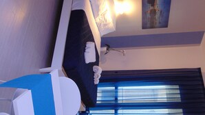 Une chambre d’hôtel avec un lit, un bureau, une chaise, une fenêtre avec des rideaux et un tableau au mur.