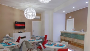 Un espace repas avec des tables et des chaises rondes, un lustre moderne et un comptoir de réception décoratif.