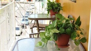 A balcony with a glass table and metal chairs, potted plants, and a tiled floor.