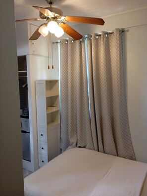 Un dormitorio con una cama, ventilador de techo y armario.