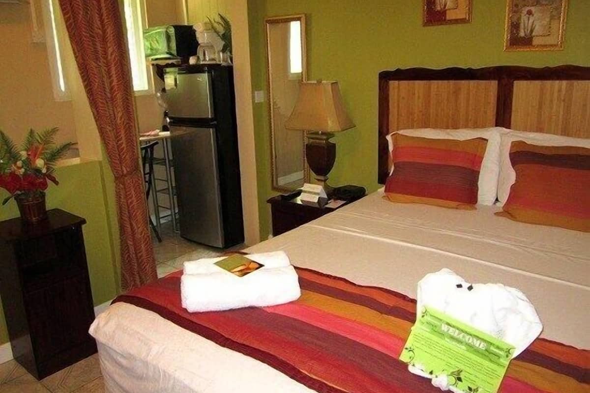 A hotel room with a bed, a nightstand, a lamp, a refrigerator, and a window with curtains.