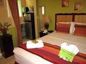 A hotel room with a bed, a nightstand, a lamp, a refrigerator, and a window with curtains.