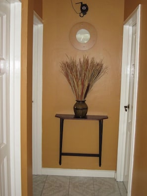 A hallway with a brown wall, a round mirror, and a vase with dried plants on a small table. - Narakiel's Inn (Roseau)
