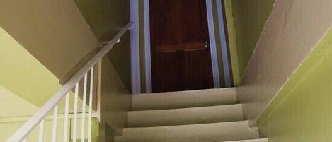 Eine Treppe mit einer Holztür am oberen Ende, weißen Geländern und einer hellen Wand.