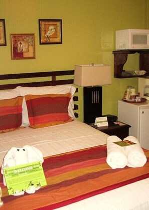 Hotelkamer met een bed, kussens, een bedlampje, een kleine koelkast en een welkomstbord.