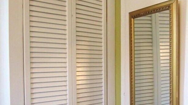 A white closet with horizontal blinds and a gold-framed mirror on the right.