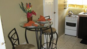 A compact kitchen with a dining table, two chairs, a stove, and a door.