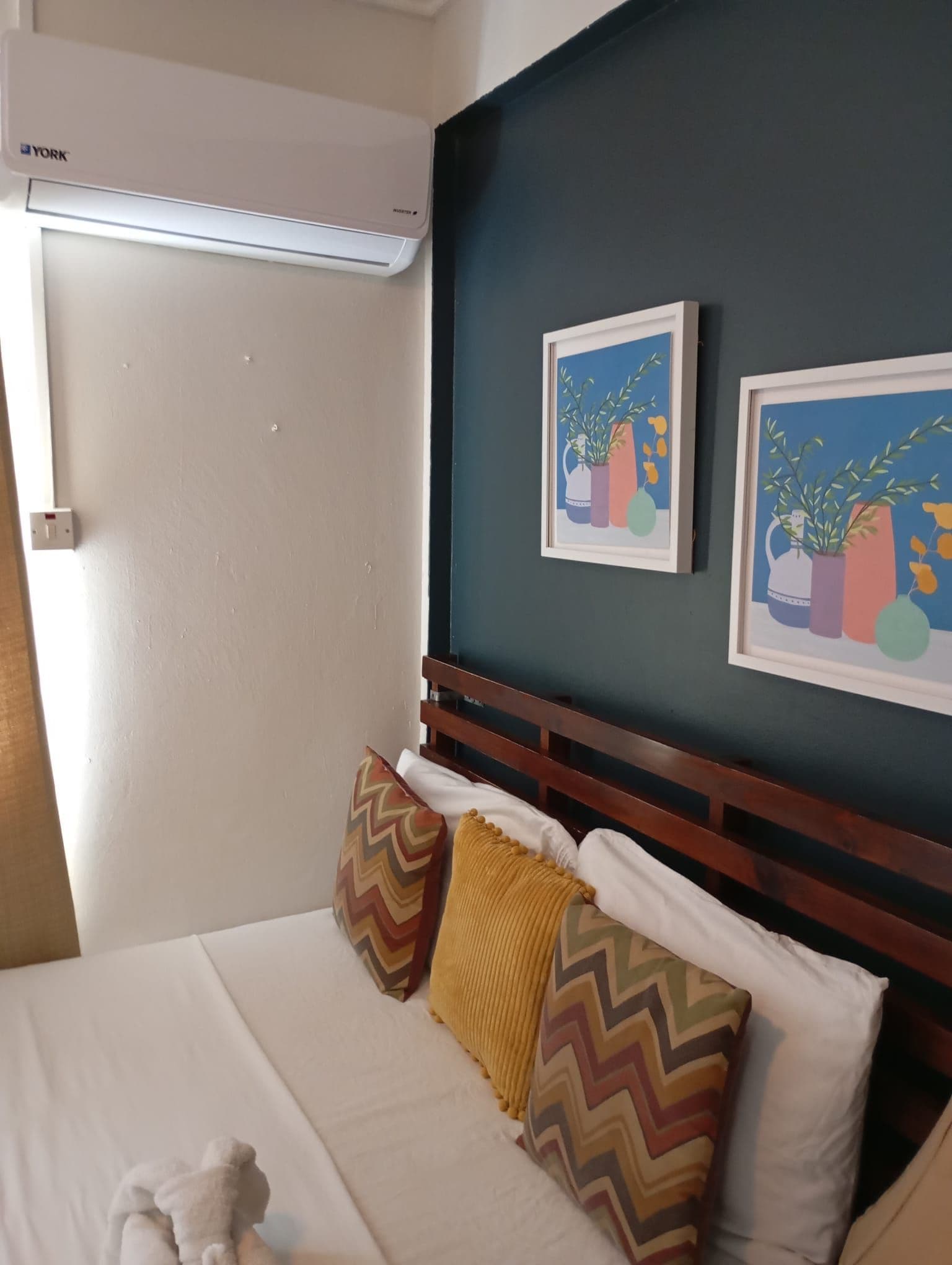 Ett hotellrum med en säng, en väggmonterad luftkonditioneringsanläggning och två inramade konstverk.