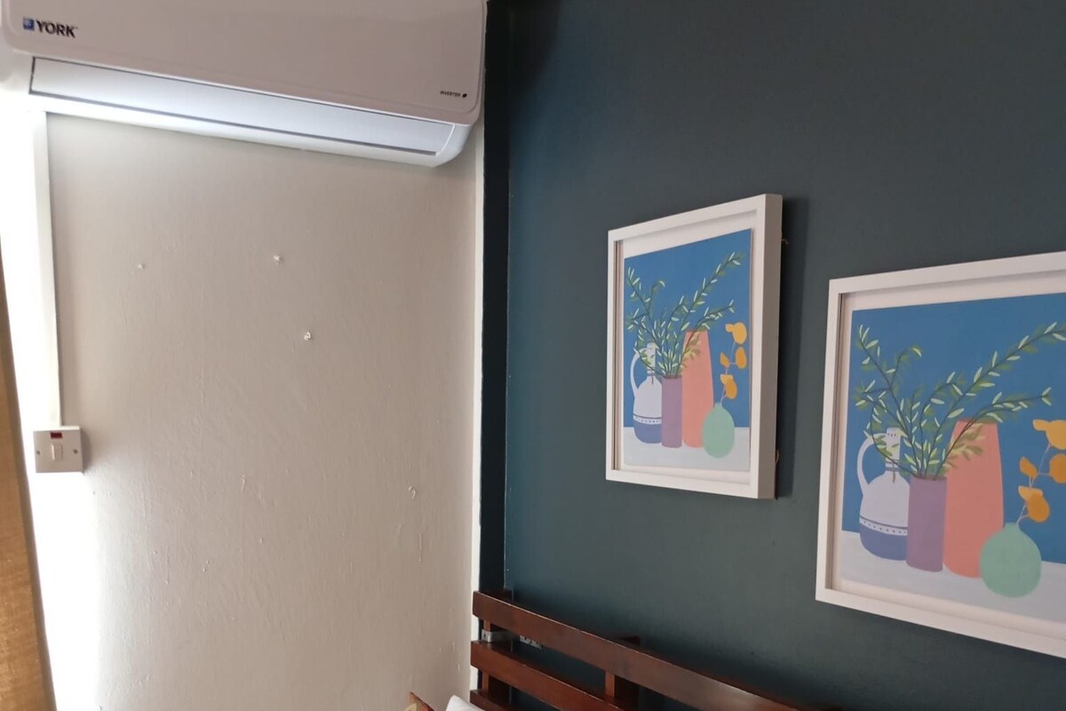 Habitación de hotel con cama, aire acondicionado de pared y dos obras de arte enmarcadas.