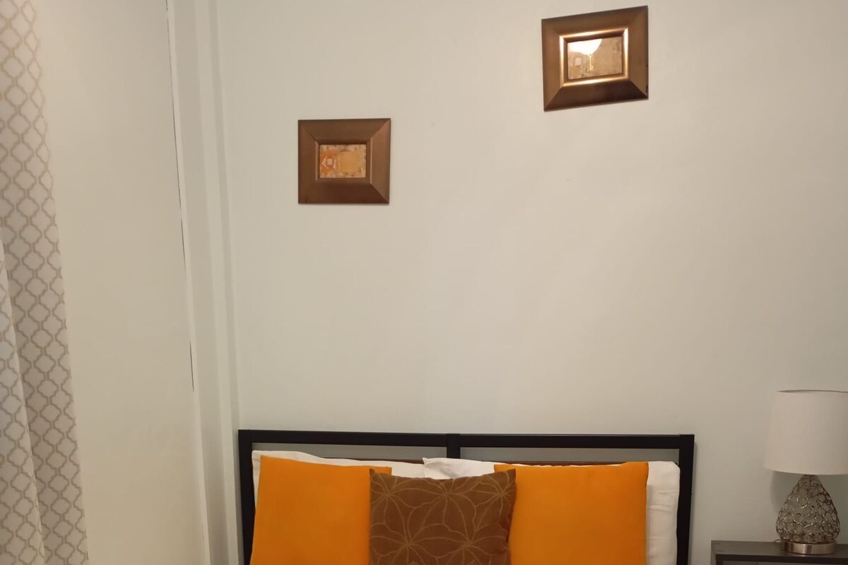 Habitación de hotel con cama, mesita de noche, lámpara y un cuadro colgado en la pared.