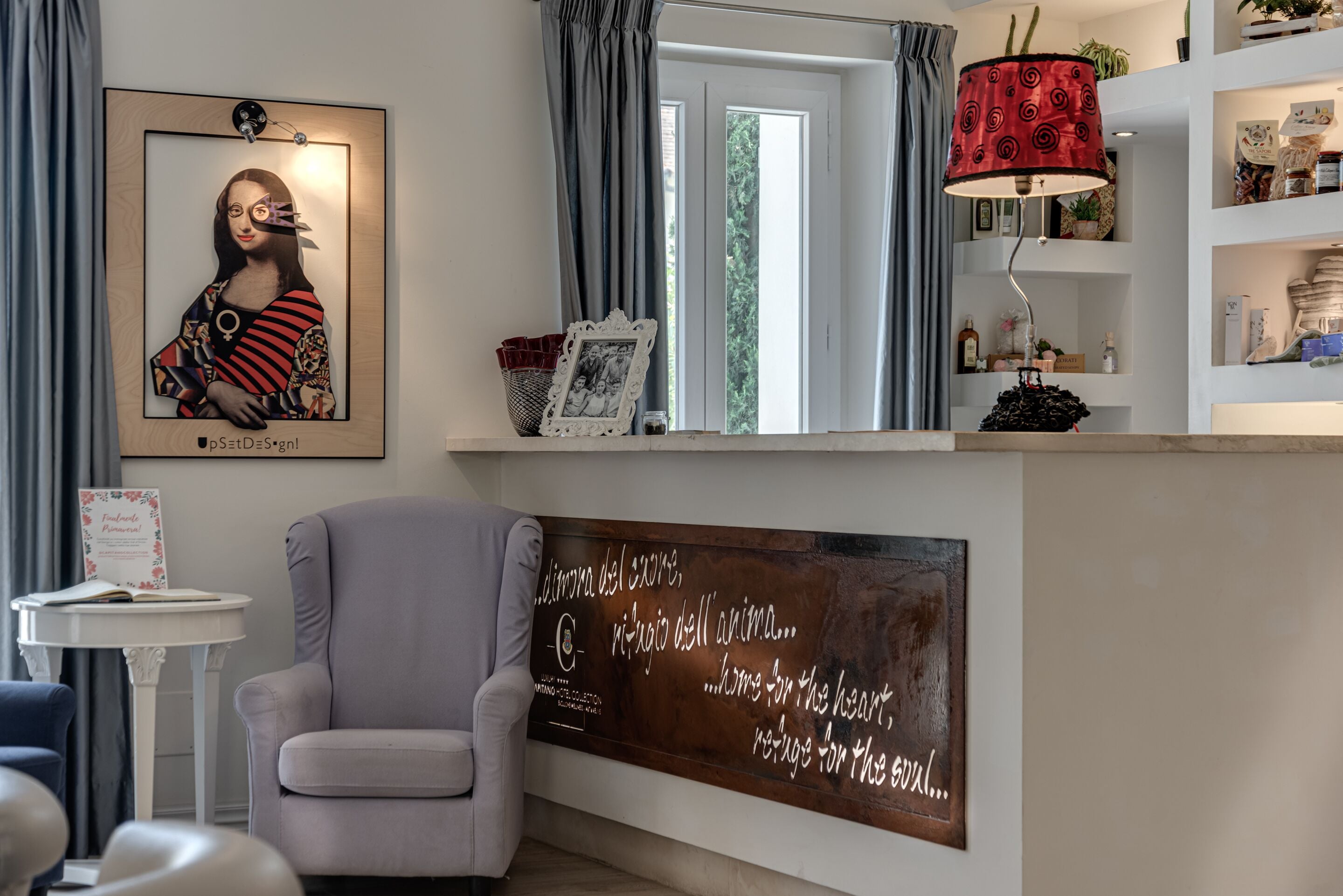 A modern living room with a grey armchair, a framed artwork, a decorative lamp, and a wall with a quote.