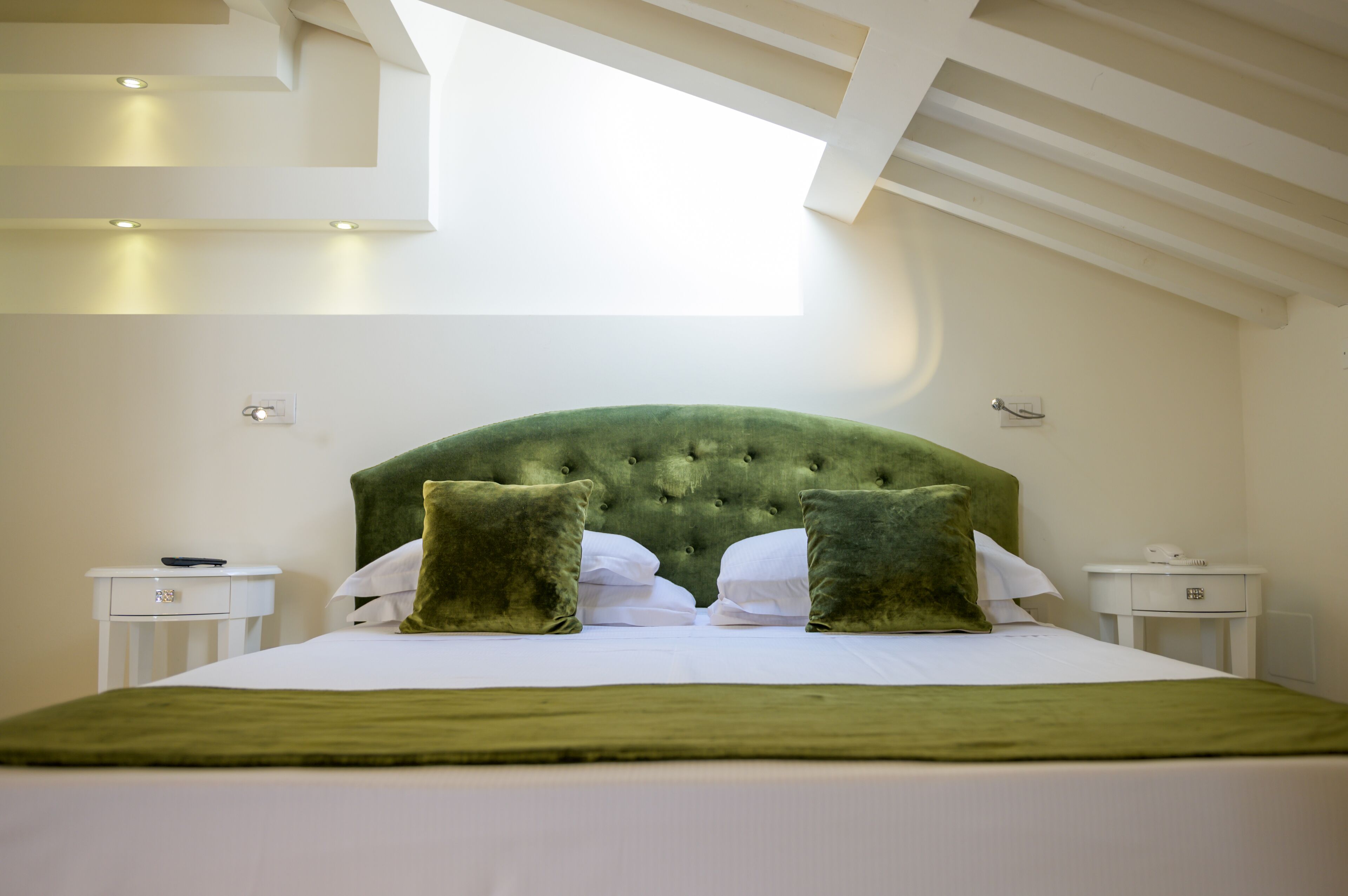 A neatly made bed with a tufted headboard, two pillows, and a green throw blanket. There are two bedside tables with a remote control on one.