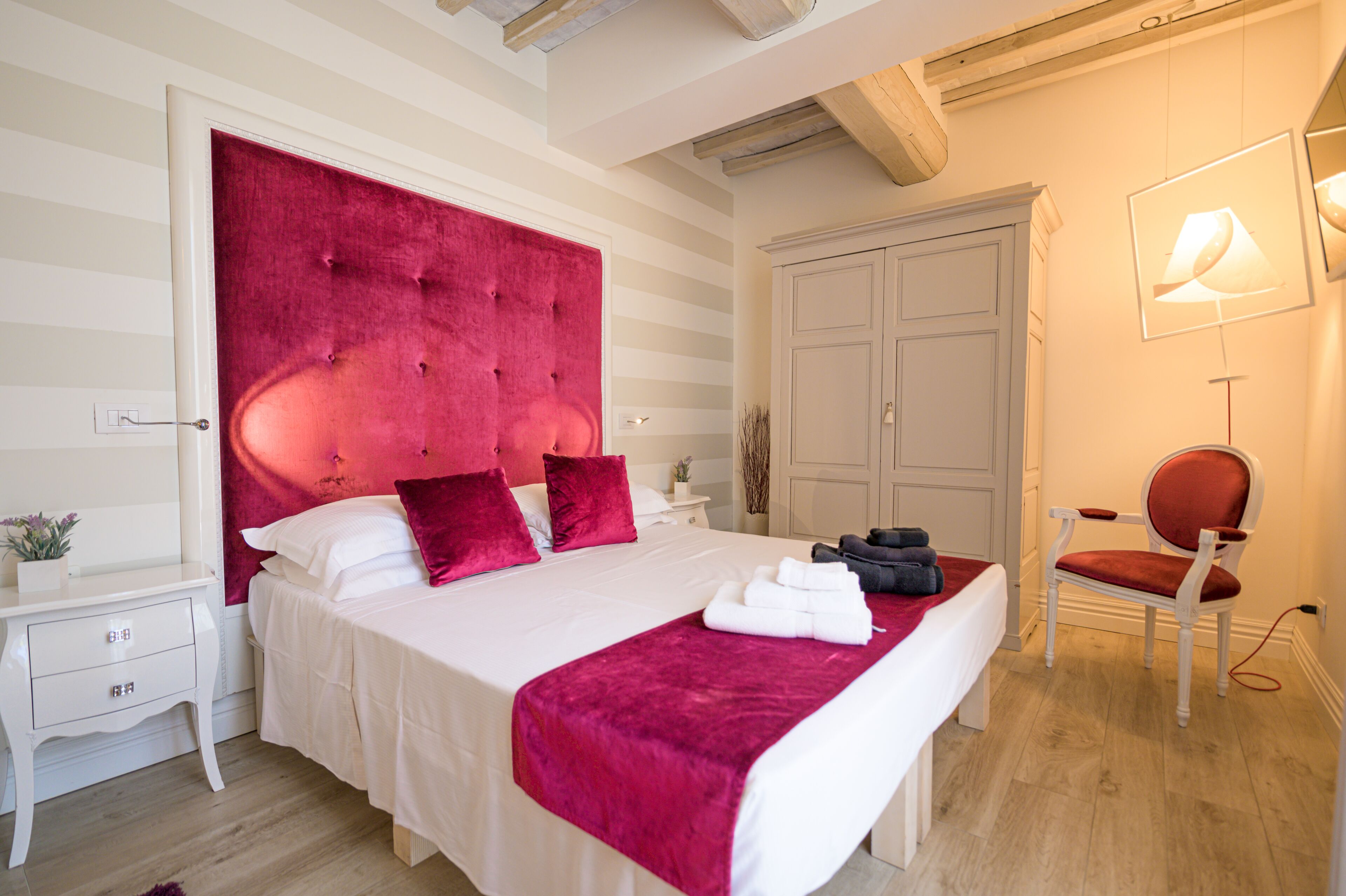 Une chambre d’hôtel avec un grand lit, une table de chevet, une armoire, une chaise et une lampe.