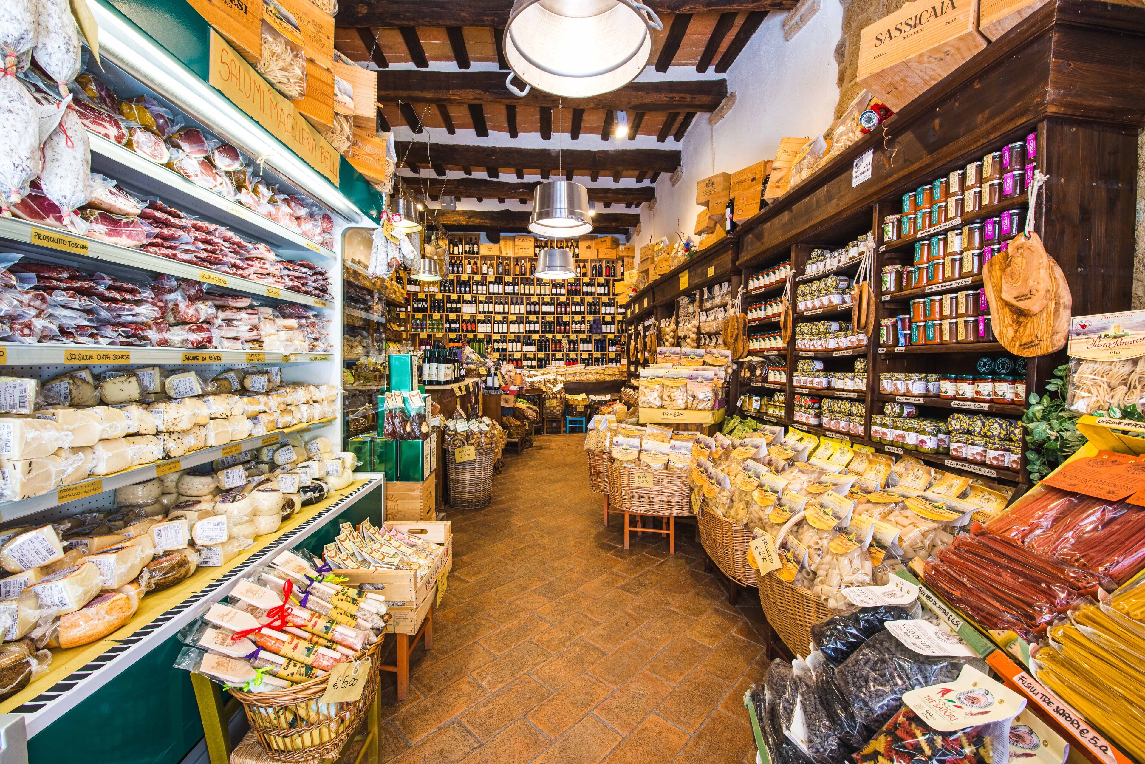 Una tienda rústica y estrecha con estantes llenos de quesos, carnes y otros productos alimenticios.