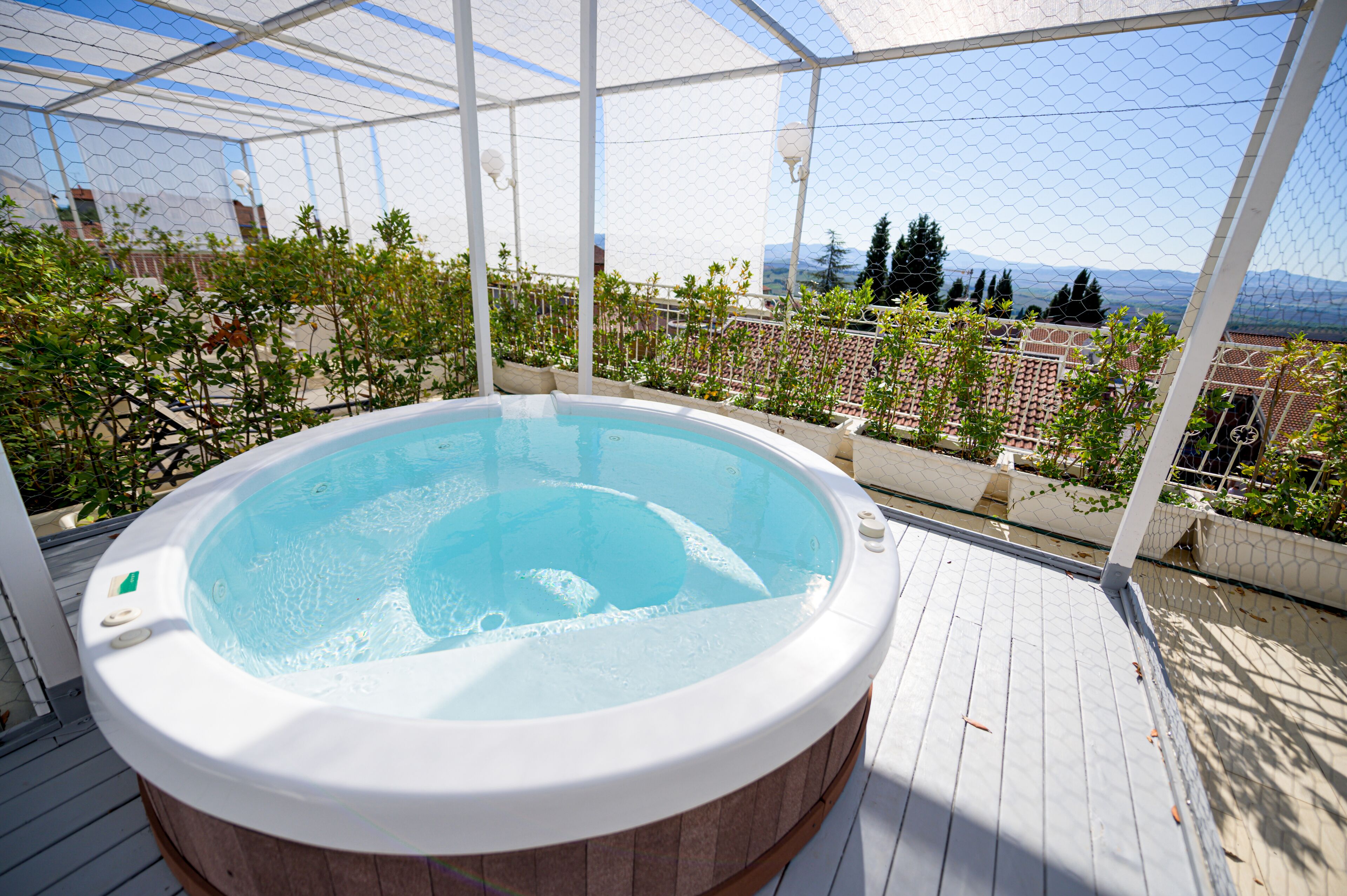 Un jacuzzi en una terraza de madera con vistas a un paisaje urbano y montañas.
