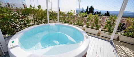 Un jacuzzi en una terraza de madera con vistas a un paisaje urbano y montañas.