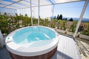 Un jacuzzi en una terraza de madera con vistas a un paisaje urbano y montañas.