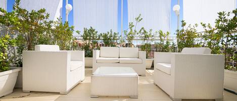 A covered outdoor seating area with white wicker furniture and potted plants.