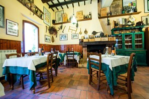 Un comedor tradicional con mesas y sillas de madera, una chimenea de ladrillo y estantes con botellas y adornos.