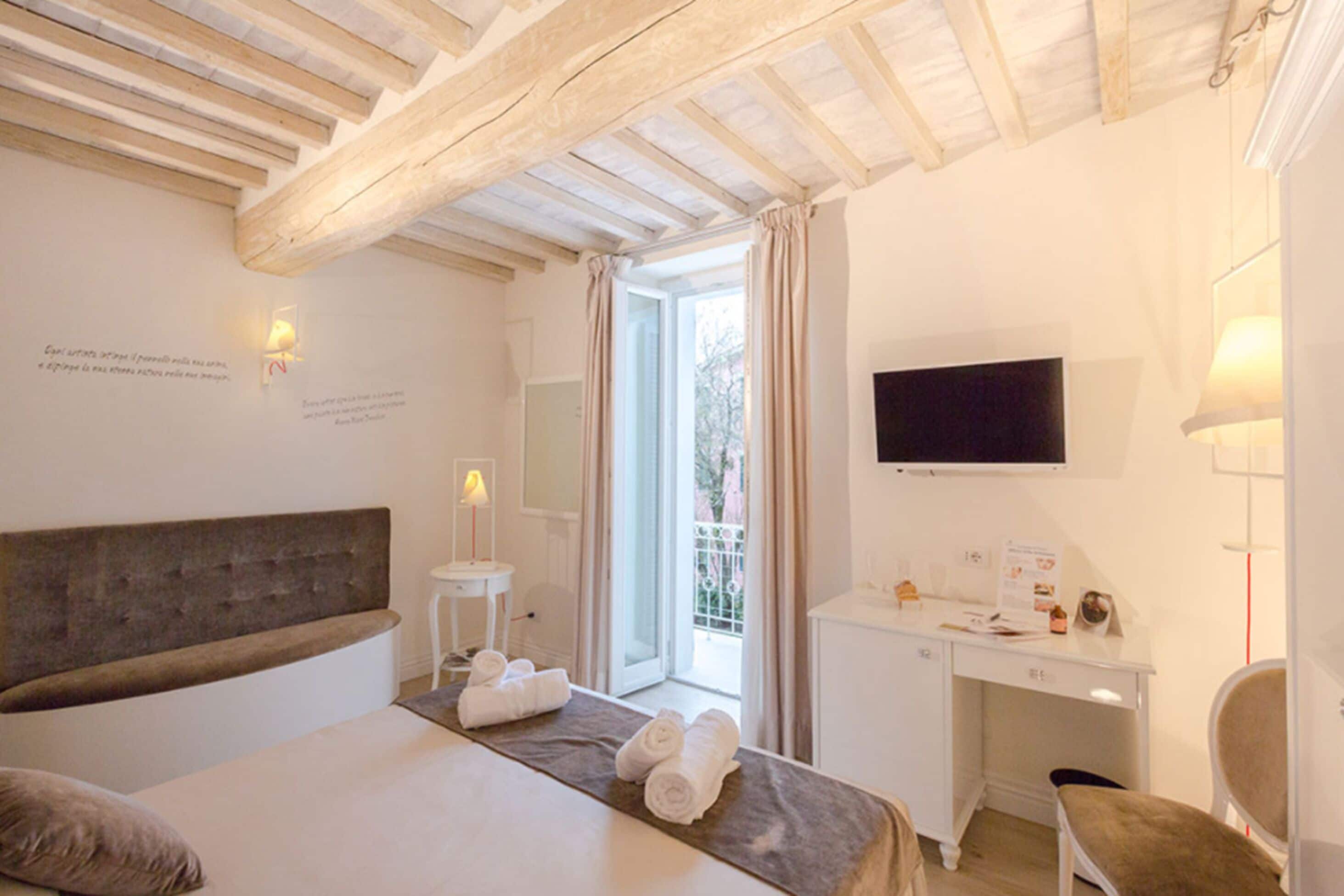 A hotel room with a bed, a desk, a chair, a TV, and a window with curtains.