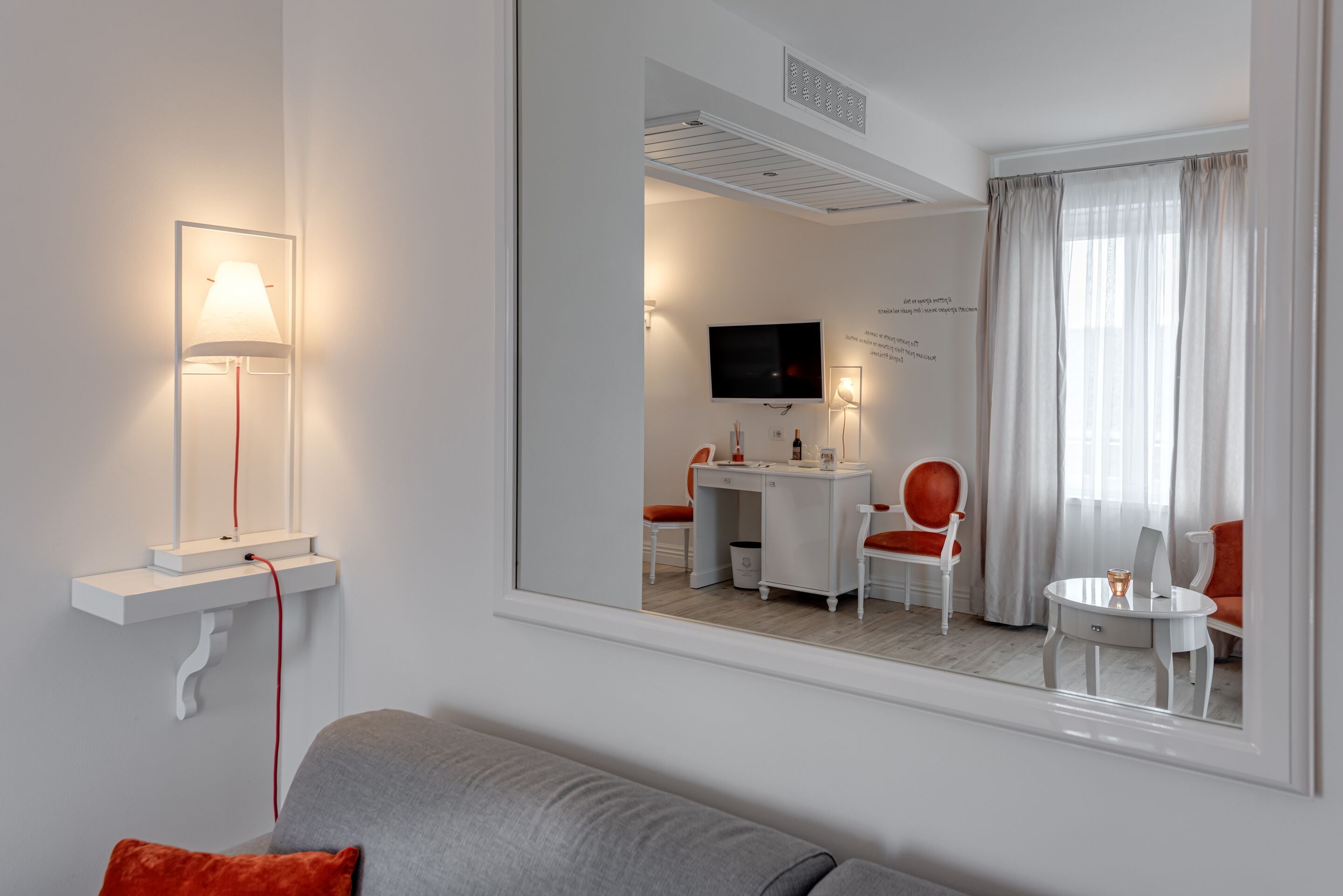 Una habitación de hotel moderna con un sofá gris, un escritorio con una silla, un televisor y una ventana con cortinas.