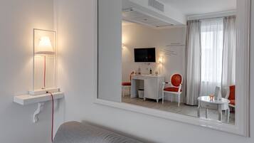 Una habitación de hotel moderna con un sofá gris, un escritorio con una silla, un televisor y una ventana con cortinas.