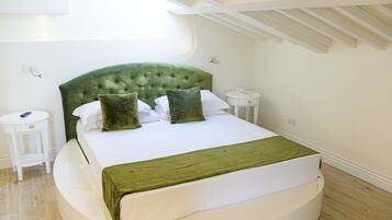 A neatly arranged bedroom with a green upholstered headboard, a round bed, white bedding, and a small bedside table with a remote control.