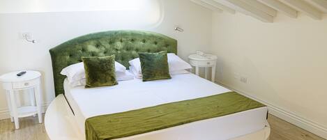 A neatly arranged bedroom with a green upholstered headboard, a round bed, white bedding, and a small bedside table with a remote control.