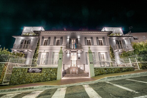 Un edificio bien iluminado de dos plantas con fachada de piedra, una entrada central con escalones y una bandera en el tejado.