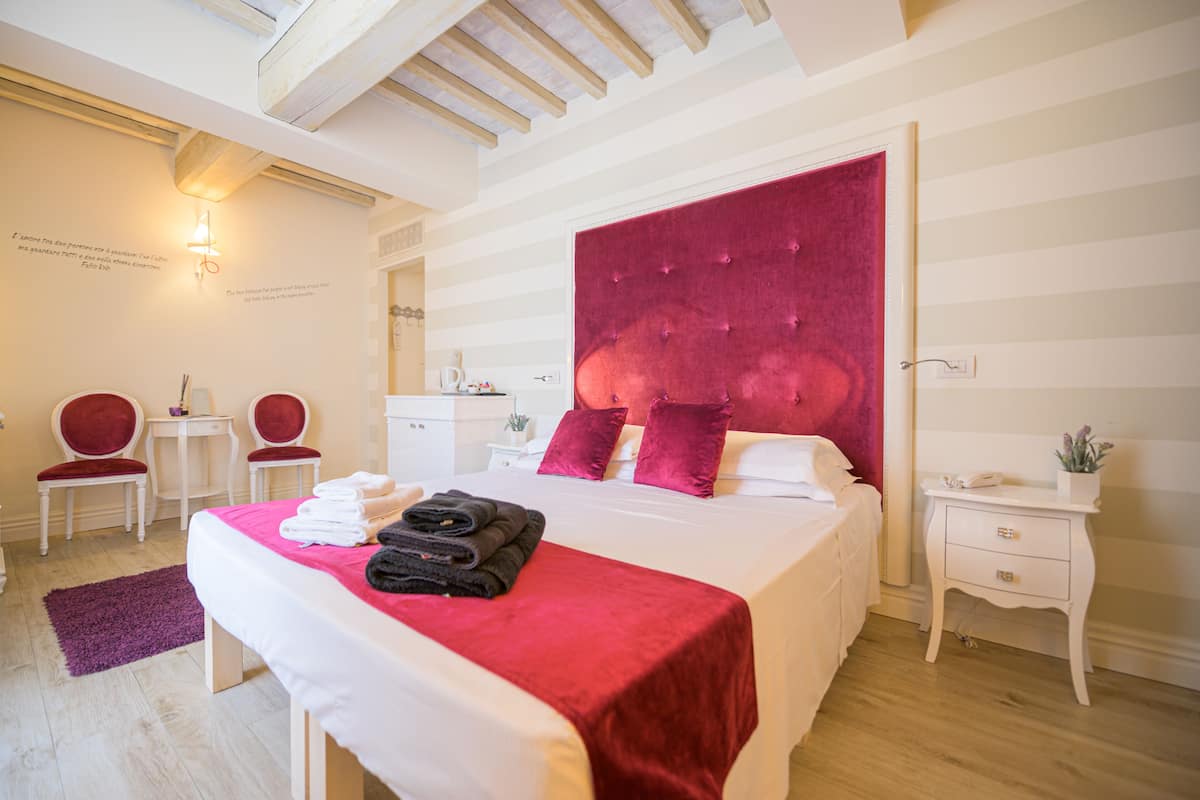 Un dormitorio con una cama grande, un cabecero rojo, dos sillas rojas, una mesita y una mesita de noche con un teléfono y una planta.
