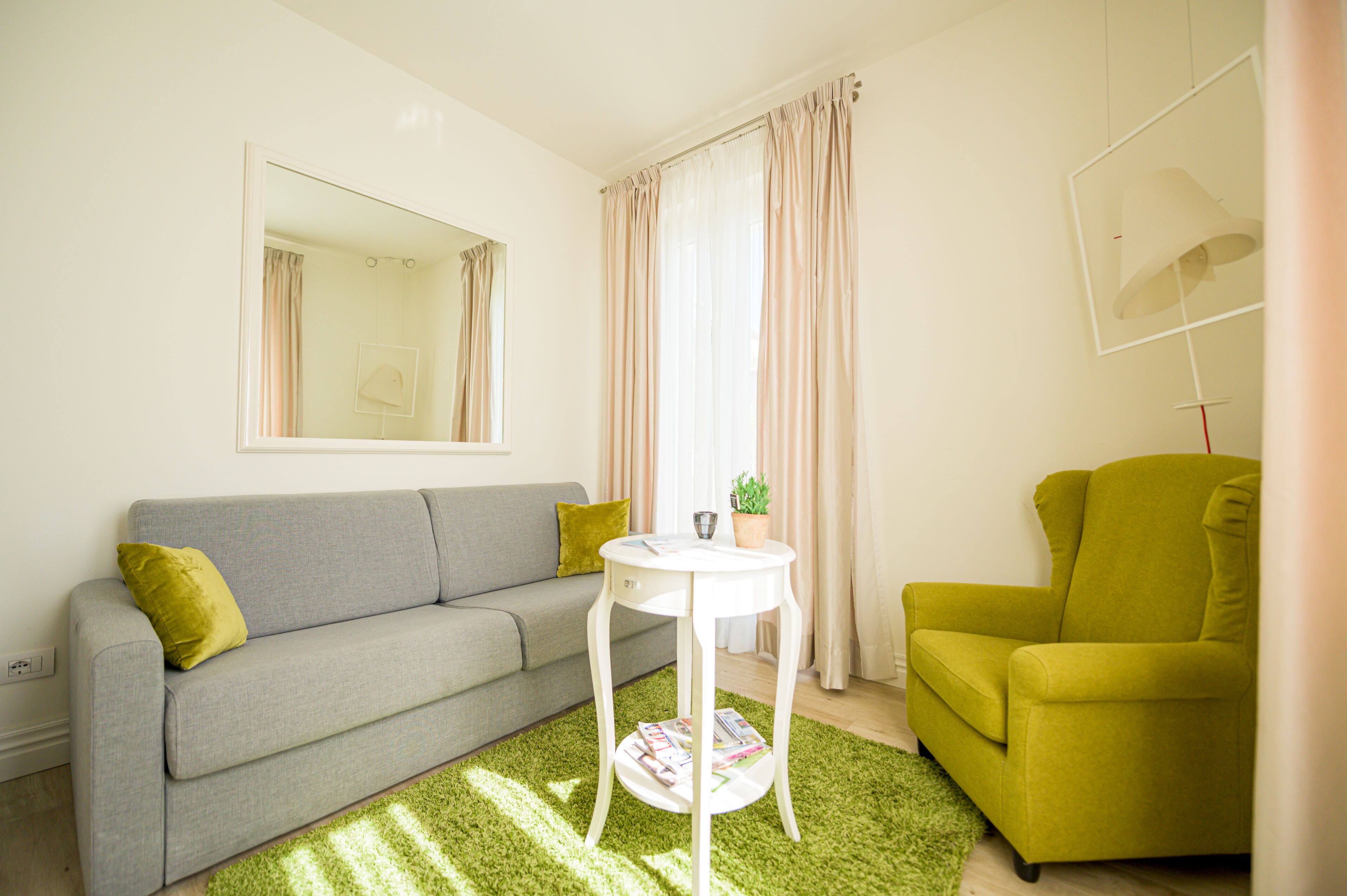 Ein Wohnzimmer mit grauem Sofa, einem grünen Sessel, einem weißen Couchtisch und einem grünen Teppich.