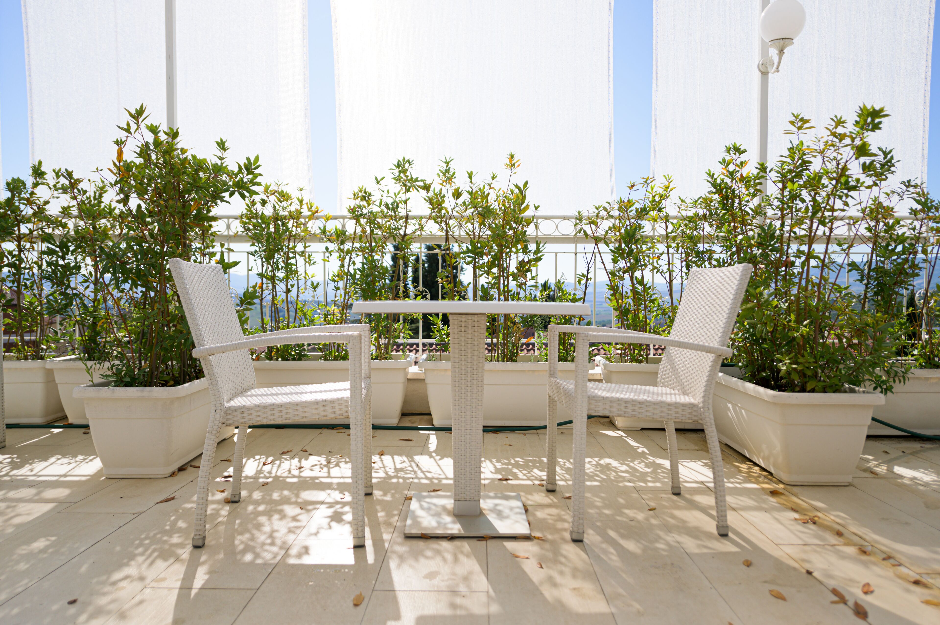 A patio with white wicker furniture and potted plants.
