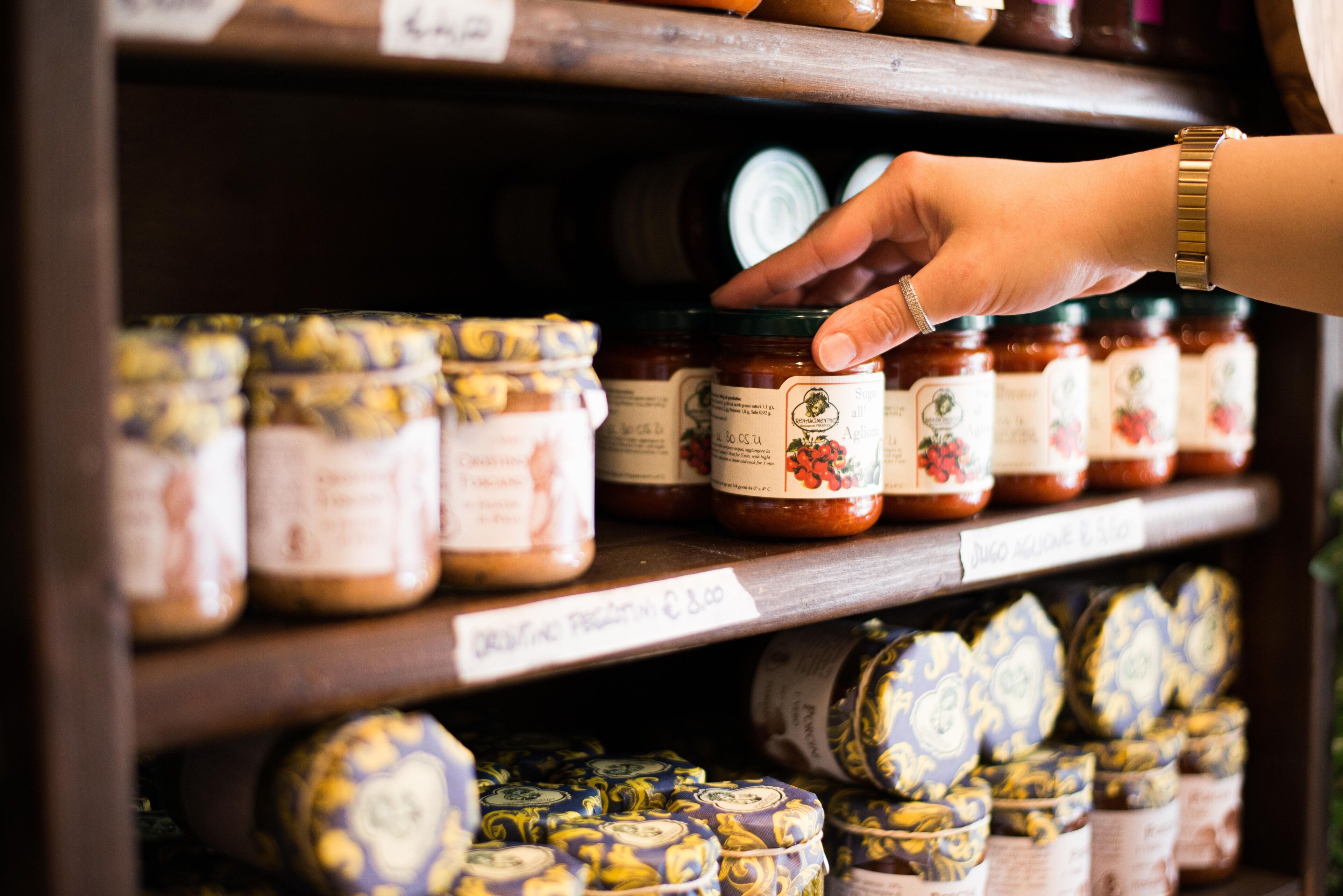 A hand reaching for a jar of jam on a shelf.