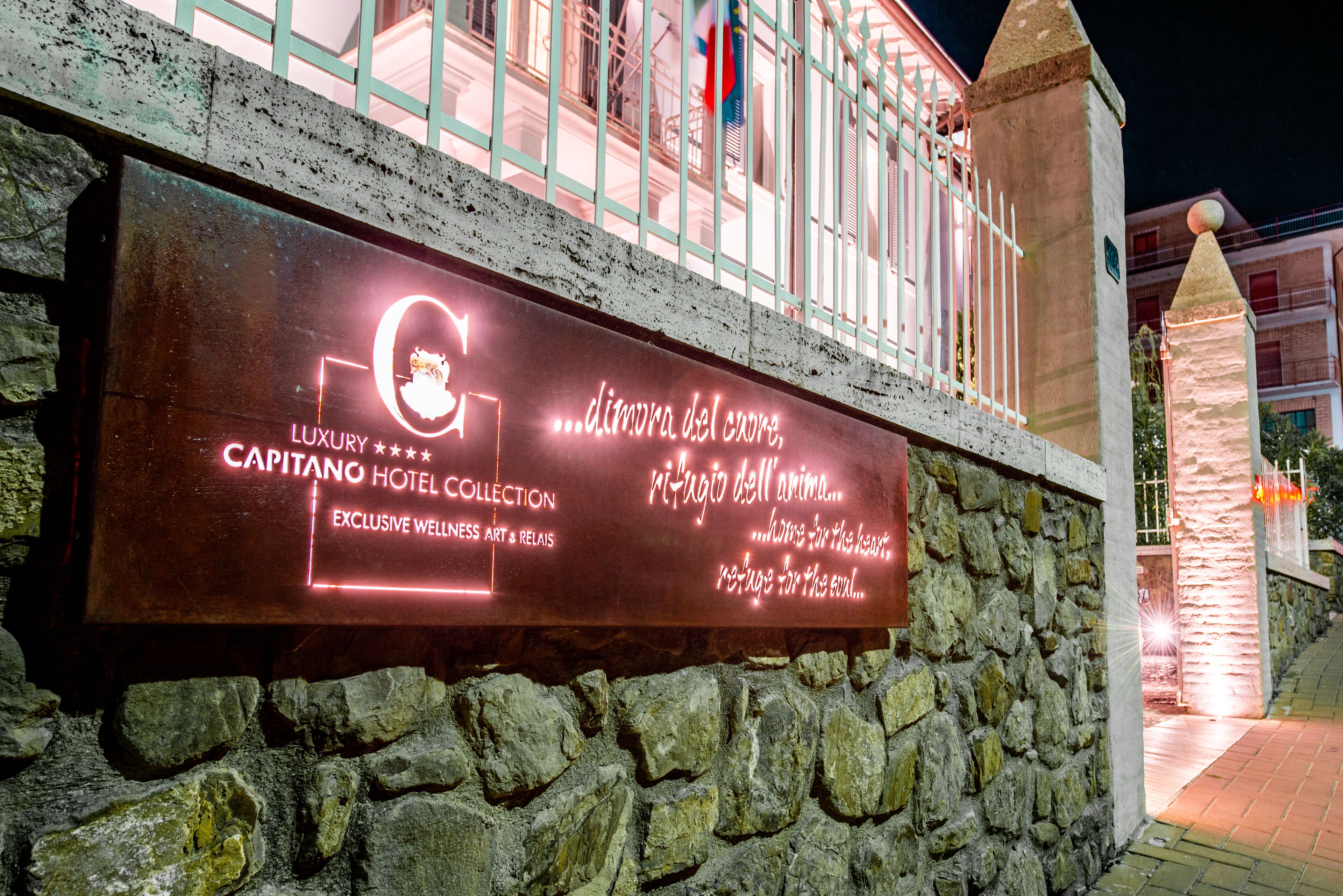A sign for the Capitano Hotel Collection with a stone wall and a balcony.