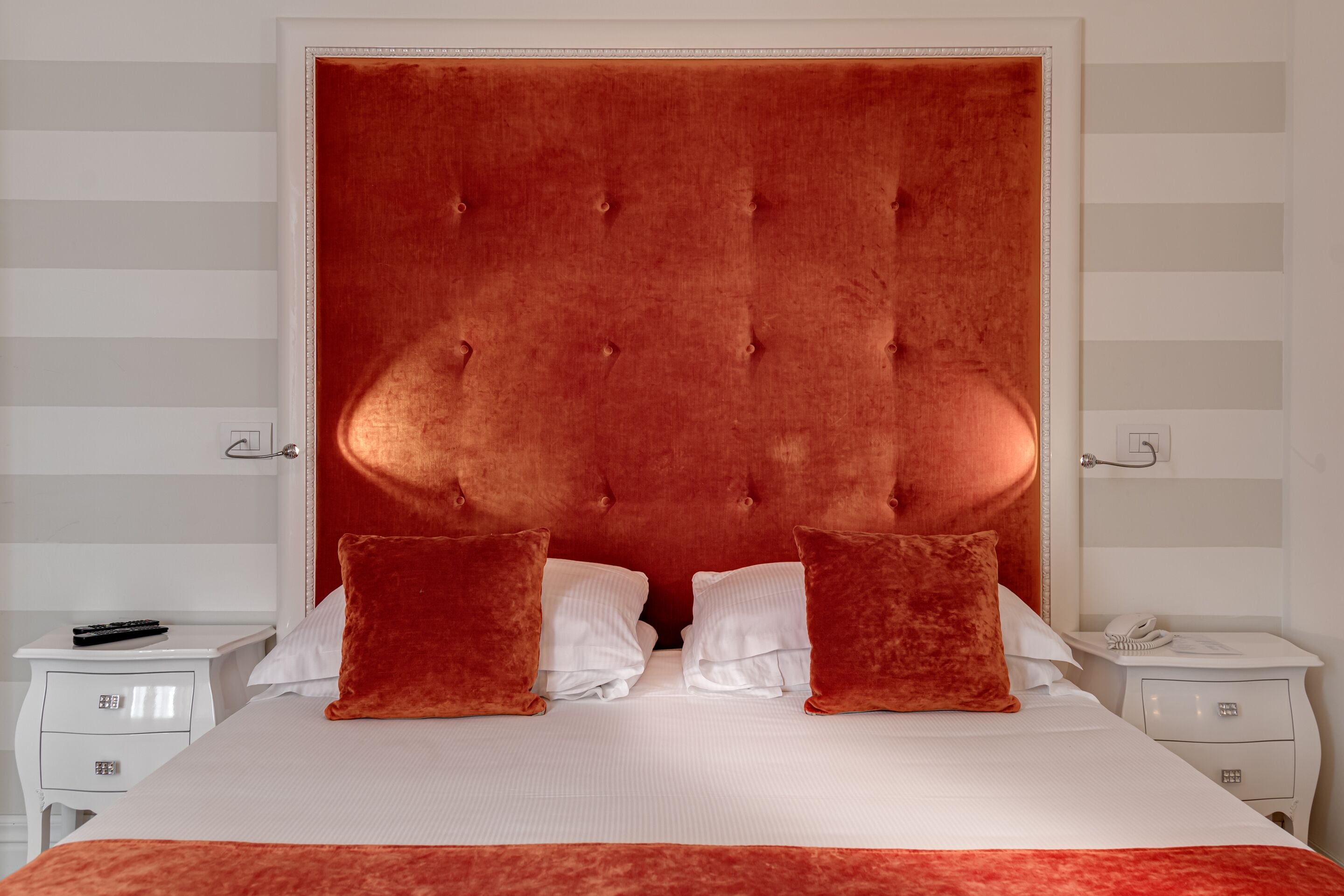 Una cama con cabecera capitonada, ropa de cama blanca y dos almohadas rojas.