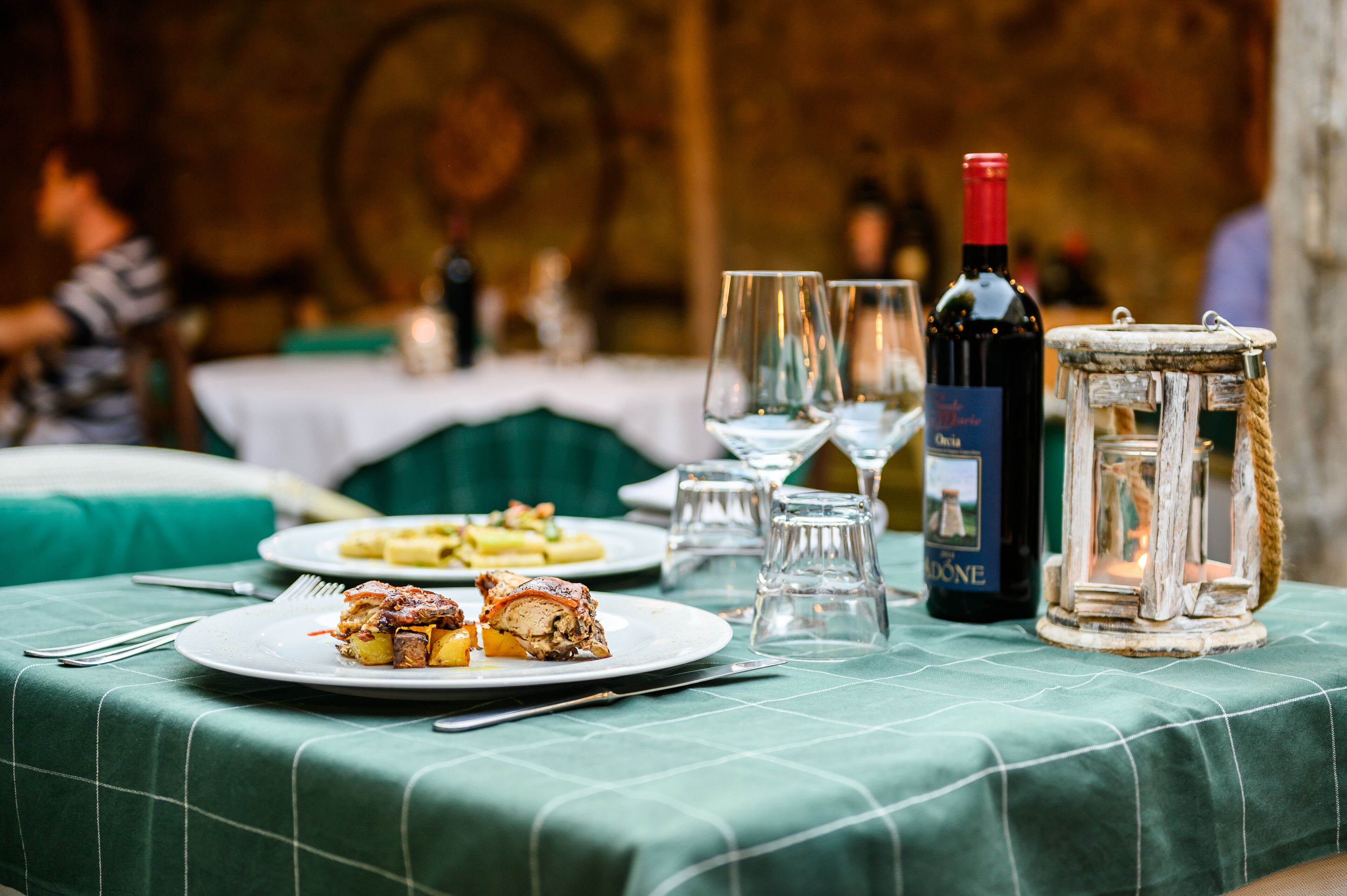 Uma mesa de jantar com pratos de comida, copos de vinho e uma garrafa de vinho.
